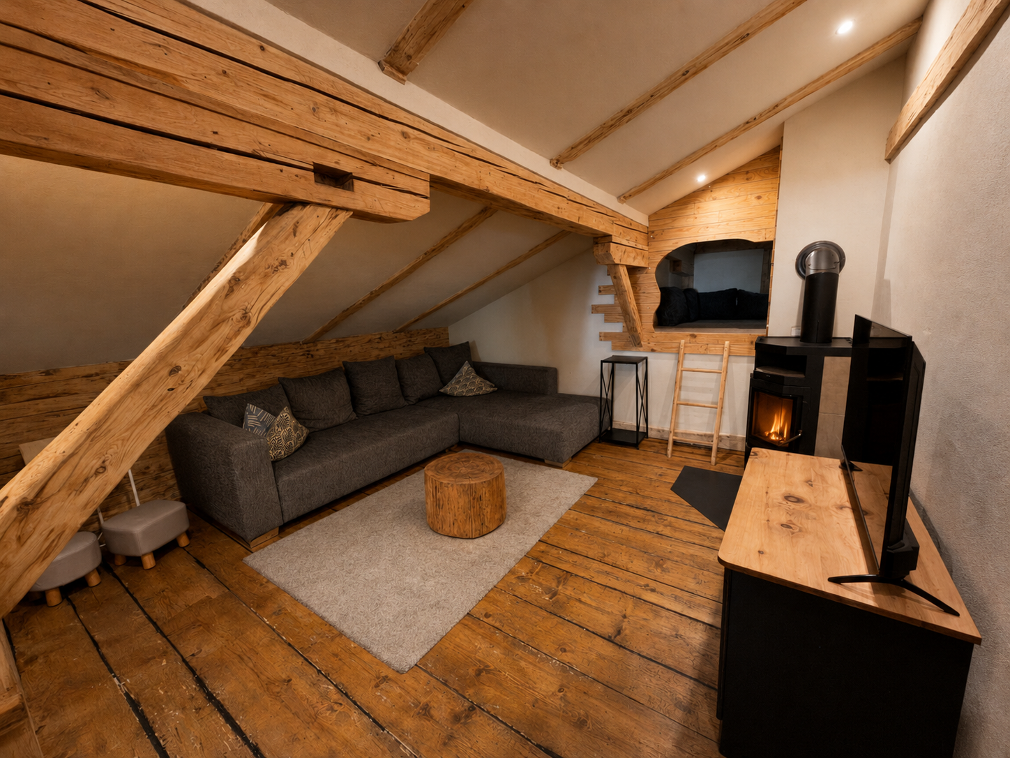 The cozy attic lounge with sofa, wood-burning stove and a sleeping nook